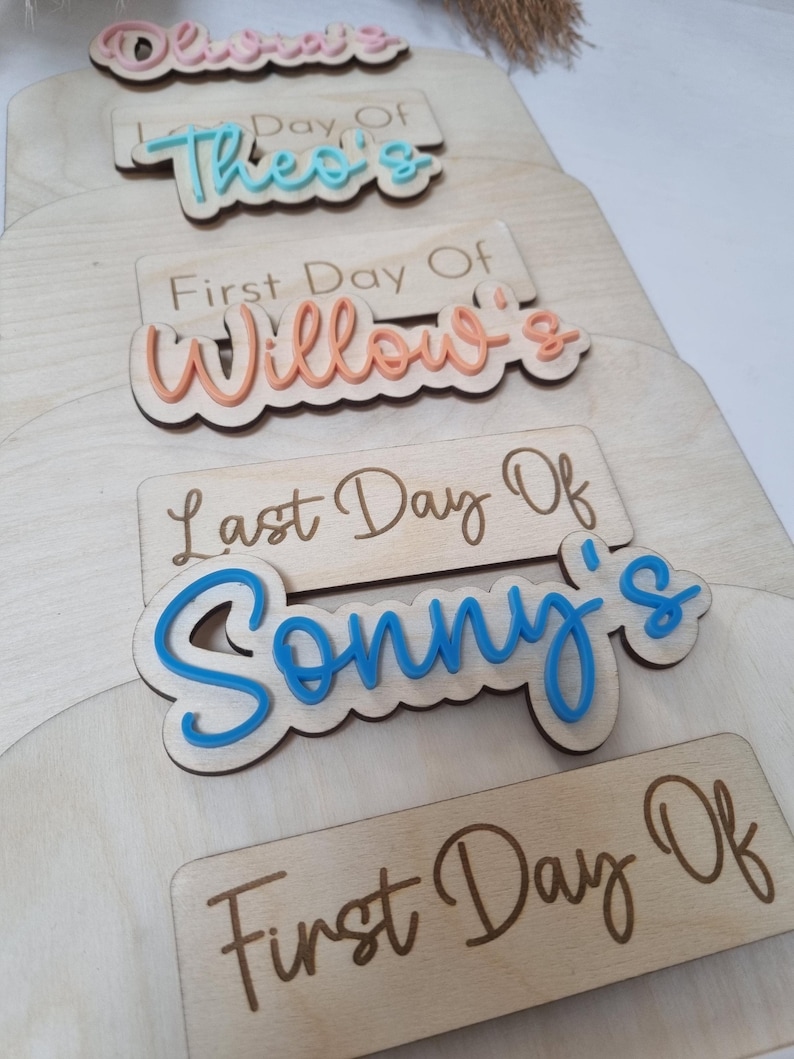 May include: Five wooden signs with the text "Day Of" and a name in a colorful script. The names are Theo's, Willow's, Sonny's, and Olivia's. The signs are stacked on top of each other.