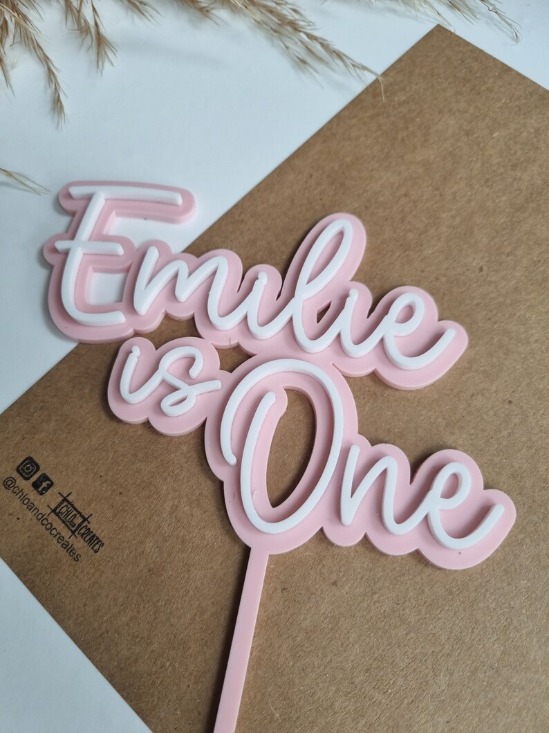 Puede incluir: Topper de pastel de acr&iacute;lico rosa y blanco con el texto "Emilie tiene un a&ntilde;o".