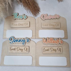 May include: Four wooden photo frames with blank spaces for pictures. Each frame has a name at the top, "Theo's", "Olivia's", "Sonny's", and "Willow's", and a sign that says "First Day Of" or "Last Day Of".