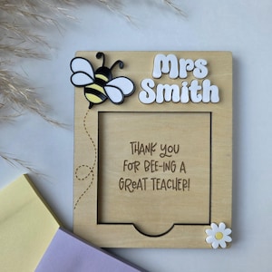 May include: Wooden plaque with a cutout for a photo, featuring a bee and daisy embellishments. The plaque reads "Mrs Smith" and "Thank you for bee-ing a great teacher!" in a playful font. A thoughtful teacher gift.