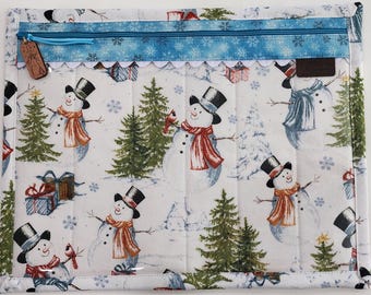 May include: A rectangular, quilted fabric pouch featuring a winter scene with snowmen, pine trees, and gift boxes. The pouch has a blue zipper and a decorative scalloped edge. The background is white with a winter landscape design.