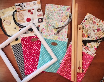 May include: A set of six fabric pouches with various floral and geometric patterns, each with a wooden tag. The pouches are arranged on a wooden surface with a white embroidery hoop and two wooden dowels.