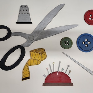 May include: A set of sewing supplies including a pair of black scissors, a thimble, a spool of yellow thread, a red pincushion with pins, a blue button, a green button, and a red button.
