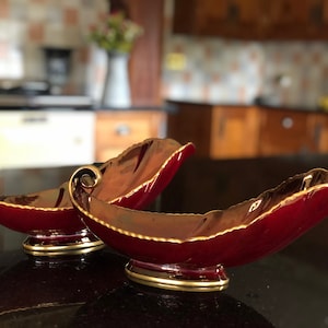 May include: Two red and gold leaf-shaped serving bowls. The bowls are made of ceramic and have a glossy finish. The bowls are decorated with gold trim and have a raised design.