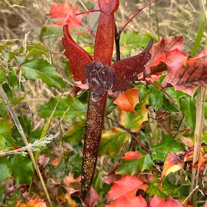 May include: A red glitter sword with a silver dragon design on the hilt. The sword is surrounded by fall foliage.