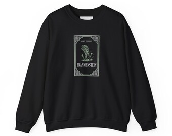 May include: Black sweatshirt featuring a graphic from Mary Shelley's "Frankenstein." The design includes a green and white illustration of a hand reaching up, with the title "Frankenstein" in white text.