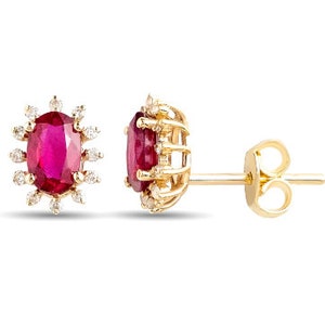 May include: A pair of gold earrings with a red oval ruby gemstone surrounded by a halo of smaller diamonds.