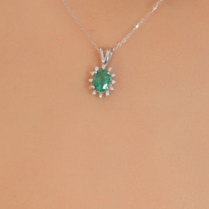 Op de afbeelding: Een delicate zilveren ketting met een hanger met een groene smaragd edelsteen omringd door kleinere diamanten.
