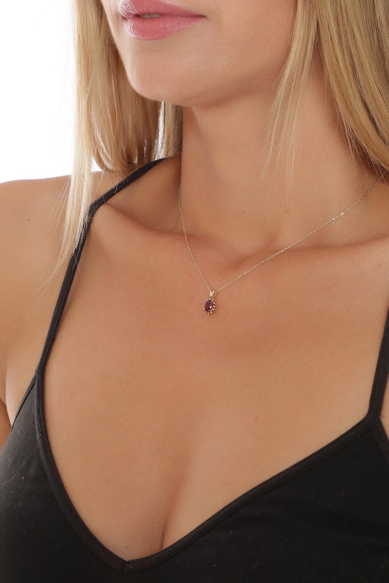 Op de afbeelding: Een gouden ketting met een klein, ovaalvormig hangertje met een rode edelsteen.