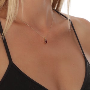 Op de afbeelding: Een gouden ketting met een rode edelsteen hanger. De hanger is gezet in een gouden halo.