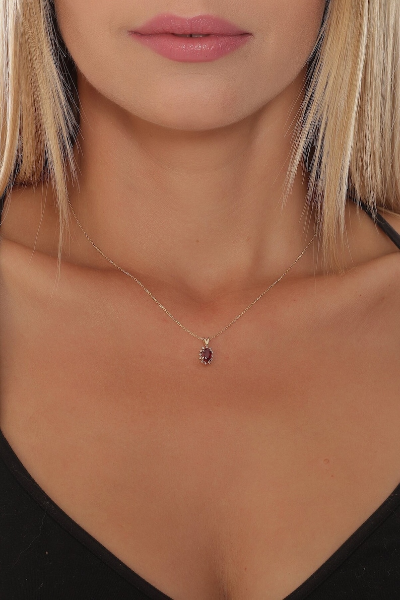 Op de afbeelding: Een gouden ketting met een klein, rond, rood edelsteen hanger.