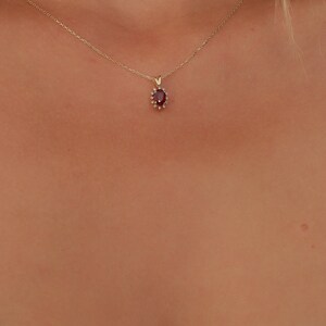 Op de afbeelding: Een gouden ketting met een rode edelsteen hanger omringd door kleinere heldere edelstenen.