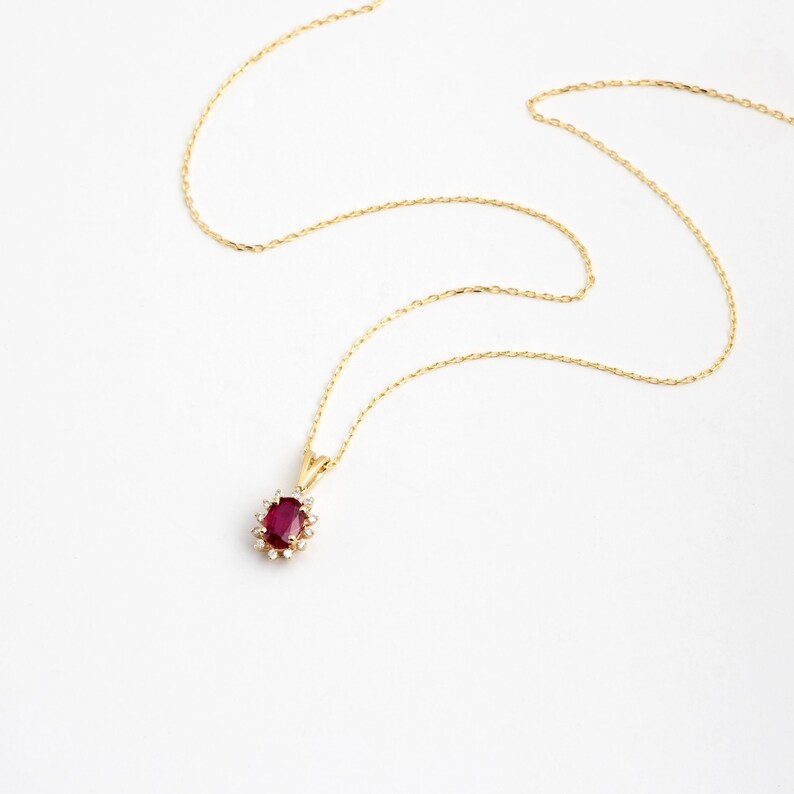 Op de afbeelding: Een gouden ketting met een hanger met een rode ovale robijn omringd door kleinere diamanten.