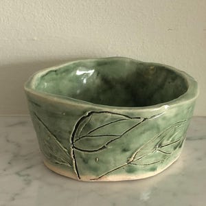 May include: A set of three ceramic mugs with a speckled, matte finish. The mugs are in shades of cream, light gray, and dark gray. Each mug has a simple, minimalist design and a rounded handle.