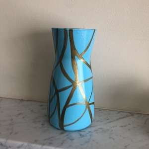 May include: A light blue vase with gold abstract lines painted on the surface.