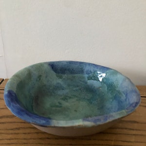 May include: A small, oval-shaped ceramic bowl with a light blue and green glaze. The bowl has a slightly uneven rim and a white interior.
