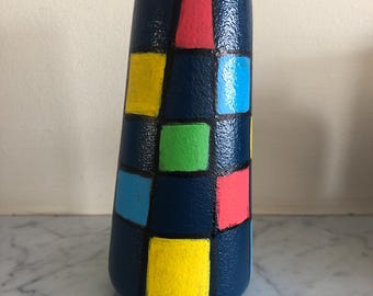 May include: A blue ceramic vase with a geometric pattern of squares in yellow, green, pink, and blue.
