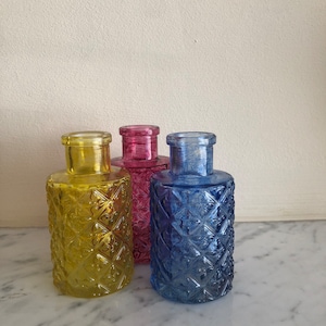 Peut inclure: Trois bouteilles en verre décoratives avec des motifs en relief. Les bouteilles sont jaunes, roses et bleues.