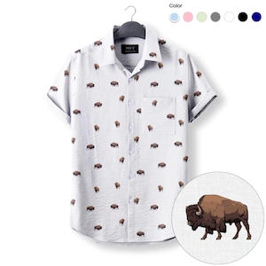 May include: A light gray short-sleeve button-down shirt featuring an all-over print of brown bison. The shirt has a standard collar, a single chest pocket on the left side, and a black inner neck label with the white text MFF.