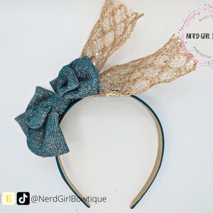 May include: Teal and gold glitter headband with a large bow and a gold glitter lace accent. The headband is made by Nerd Girl Bowtique.