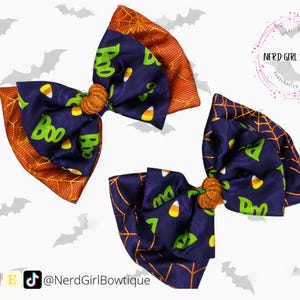 Puede incluir: Tres lazos para el pelo con tem&aacute;tica de Halloween. Los lazos presentan una tela azul marino con caramelos de ma&iacute;z y la palabra "Boo" en verde. Los bordes son naranjas con un dise&ntilde;o de telara&ntilde;a. El centro de cada lazo tiene una peque&ntilde;a calabaza naranja.