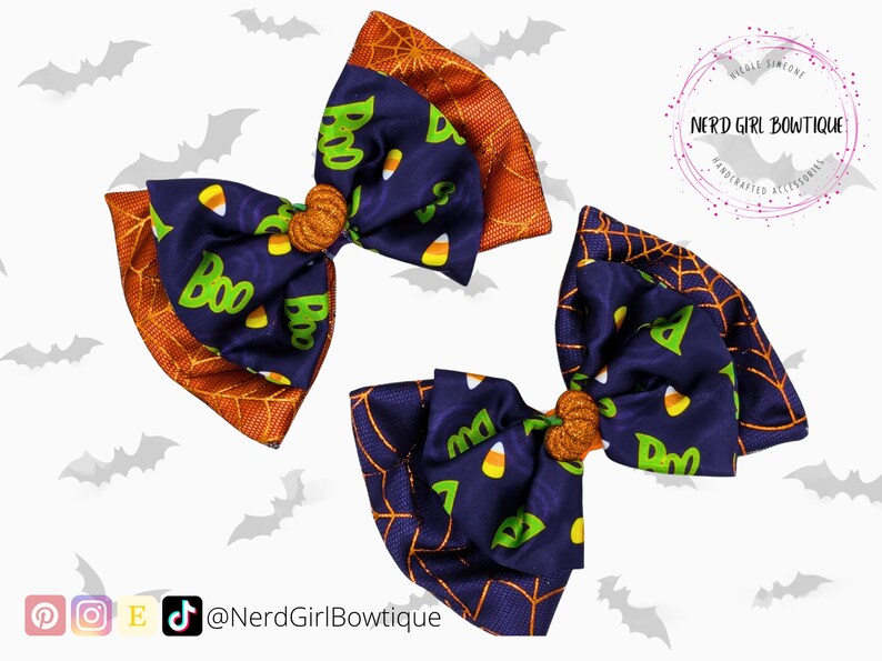 Puede incluir: Tres lazos para el pelo con tem&aacute;tica de Halloween. Los lazos presentan una tela azul marino con caramelos de ma&iacute;z y la palabra "Boo" en verde. Los bordes son naranjas con un dise&ntilde;o de telara&ntilde;a. El centro de cada lazo tiene una peque&ntilde;a calabaza naranja.