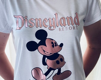 May include: White t-shirt with a rose gold Disneyland Resort logo and a rose gold Mickey Mouse graphic.