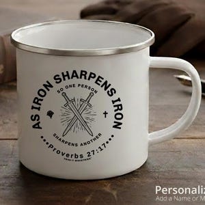 May include: White enamel mug with a silver rim and handle. The mug features the text "AS IRON SHARPENS IRON" in a circular design, with crossed swords and the Bible verse Proverbs 27:17.