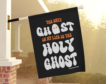 Puede incluir: Una bandera de jardín rectangular negra con texto en blanco y naranja que dice: THE ONLY GHOST IN MY LIFE IS THE HOLY GHOST. La letra O en la palabra GHOST está reemplazada por una pequeña ilustración de un fantasma blanco con ojos naranjas.