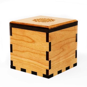 May include: A small wooden box with a decorative design on the top. The box is made of light wood with dark wood trim.