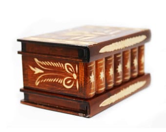 May include: A wooden puzzle box with a brown finish and intricate carvings. The box is shaped like a stack of books and has a sliding mechanism to open it.