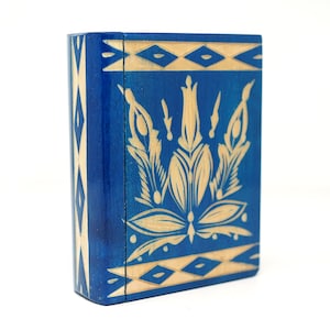 Peut inclure: Une petite boîte en bois avec un extérieur peint en bleu et un motif floral sculpté dans un bois plus clair. La boîte a un couvercle à charnière et une bordure décorative.