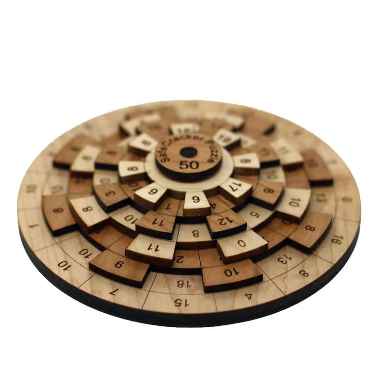 Puede incluir: Un rompecabezas circular de madera con un disco central etiquetado como "Safe Cracker Puzzle" y "50". El rompecabezas tiene m&uacute;ltiples anillos conc&eacute;ntricos con n&uacute;meros del 0 al 18.
