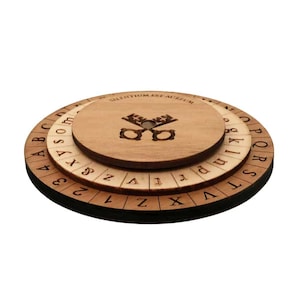 May include: A wooden cipher wheel with three rotating layers. The top layer features the text "SILENTIUM EST AUREUM" and a key design. The middle and bottom layers have letters and numbers. The wheel is made of light brown wood.