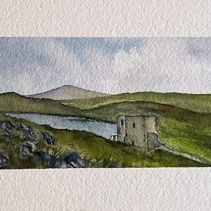 Puede incluir: Pintura acuarela de una torre de piedra en una colina con vistas a un lago. El cielo es de color azul claro con nubes blancas. Las colinas son verdes y el lago es de color azul claro.