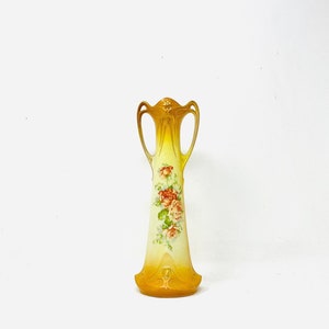 May include: A yellow and white ceramic vase with a floral design. The vase has two handles and a slender, elongated body.