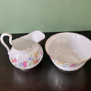 May include: A white porcelain creamer and sugar bowl set with a floral pattern. The creamer has a handle and a scalloped edge. The sugar bowl is round with a scalloped edge.