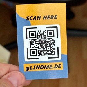 Könnte beinhalten: Eine rechteckige Karte mit einem QR-Code, dem Text "SCAN HERE" in Schwarz und dem Text "@LINDME.DE" in Gelb. Die Karte hat ein gelb-blaues Farbschema.