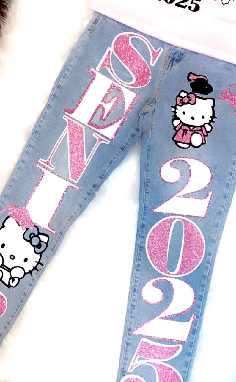 May include: A pair of blue denim jeans with pink glitter lettering that says "SENI 2025" and a pink glitter Hello Kitty graphic with a graduation cap.