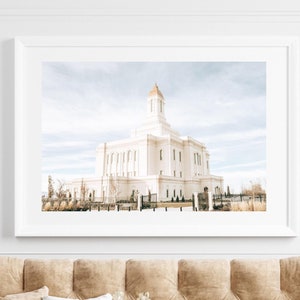 Könnte beinhalten: Ein gerahmtes Foto eines weißen Tempels mit blauem Himmel und Wolken im Hintergrund. Der Tempel ist von Bäumen und Gras umgeben. Das Foto hängt an einer weißen Wand über einem braunen Sofa.