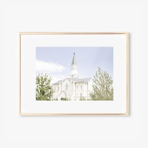 Puede incluir: Una fotografía enmarcada de una iglesia blanca con un alto campanario contra un cielo azul con nubes blancas. La iglesia está rodeada de árboles verdes.