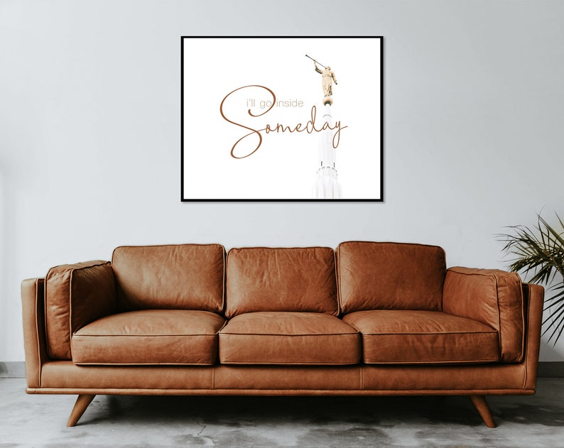 May include: A white framed print with a brown text overlay that reads "I'll go inside someday". The text is in a cursive font. The image in the print is a white building with a golden statue of an angel on top. The angel is holding a trumpet.