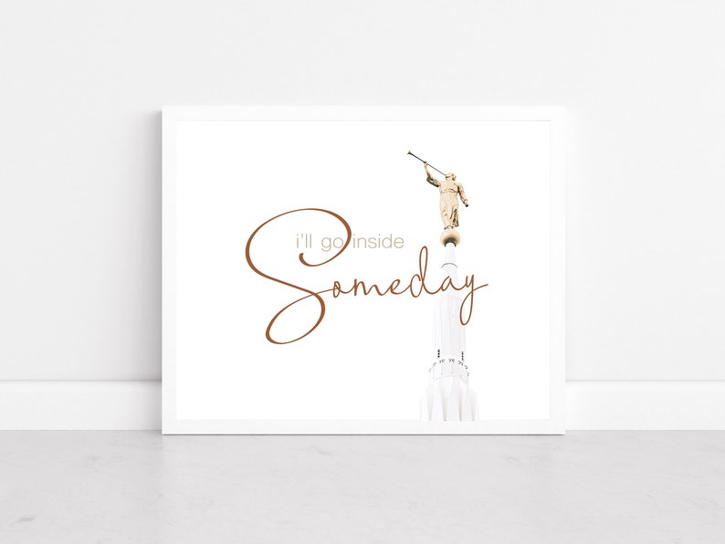 May include: A white framed print with a brown inscription that reads "I'll go inside someday". The inscription is in a cursive font. The print features a black and white photograph of a tall, white building with a golden statue of an angel on top. The angel is holding a trumpet.
