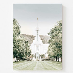 May include: A photograph of a white temple with a gold statue on top, framed by trees and a green lawn. The temple is centered, with a mountain range in the background and a pale blue sky.