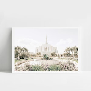 May include: A framed print of a white building with a tall spire, set against a light blue sky. The building is surrounded by lush greenery, including palm trees and flowering plants. The image has a soft, pastel color palette.