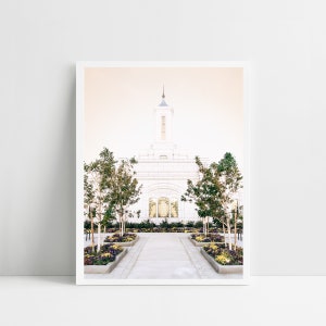 May include: A white temple with a tall spire, surrounded by a garden with green trees and colorful flowers. The temple has a walkway leading to the entrance.
