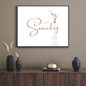 May include: A framed print with a white background featuring a golden statue of an angel holding a trumpet. The text "I'll go inside someday" is written in brown cursive script.