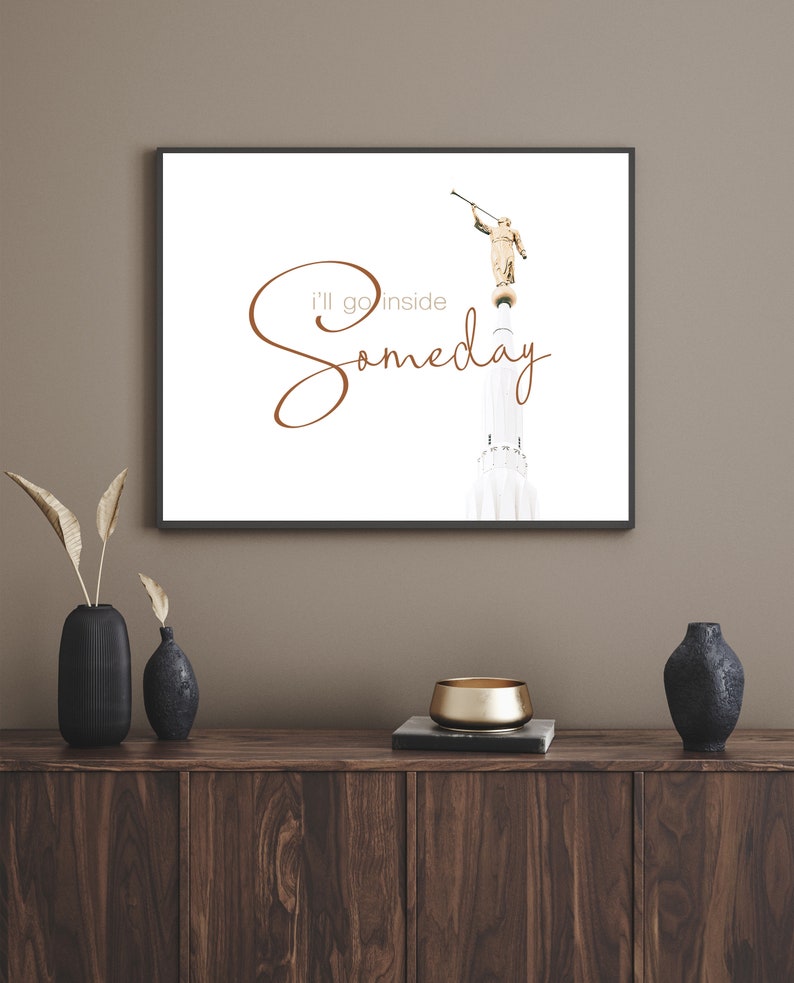 May include: A framed print with a white background featuring a golden statue of an angel holding a trumpet. The text "I'll go inside someday" is written in brown cursive script.