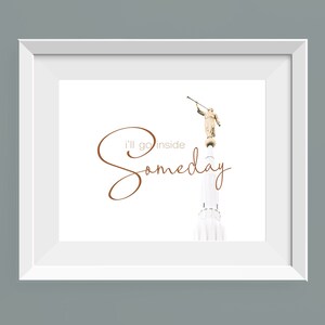 May include: A white framed print with a brown cursive inscription that reads "I'll go inside someday". The print features a photograph of a white building with a golden statue of an angel on top.