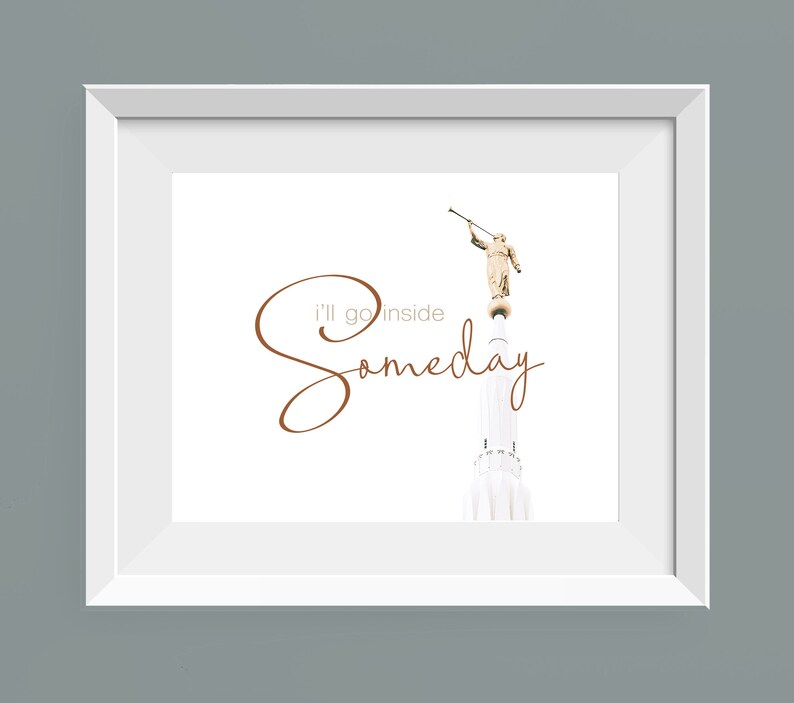 May include: A white framed print with a brown cursive inscription that reads "I'll go inside someday". The print features a photograph of a white building with a golden statue of an angel on top.